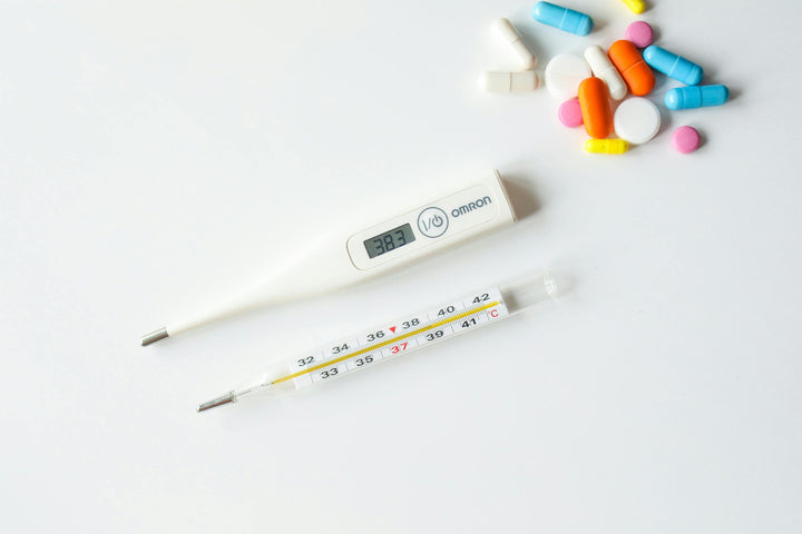 Thermometer and medicine on a white surface representing fever and flu treatment