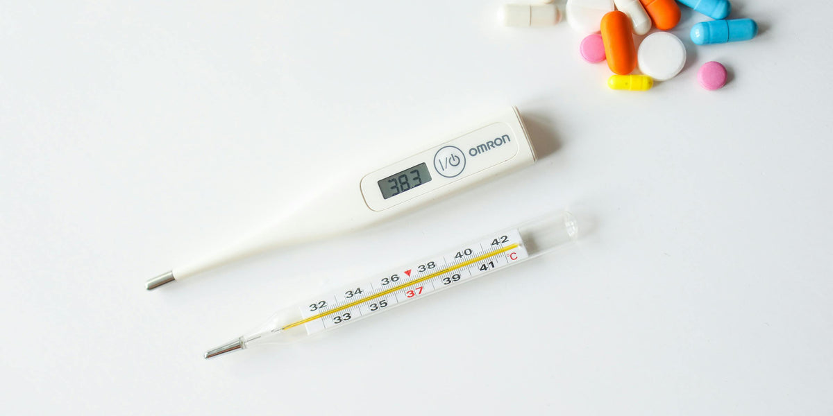 Thermometer and medicine on a white surface representing fever and flu treatment